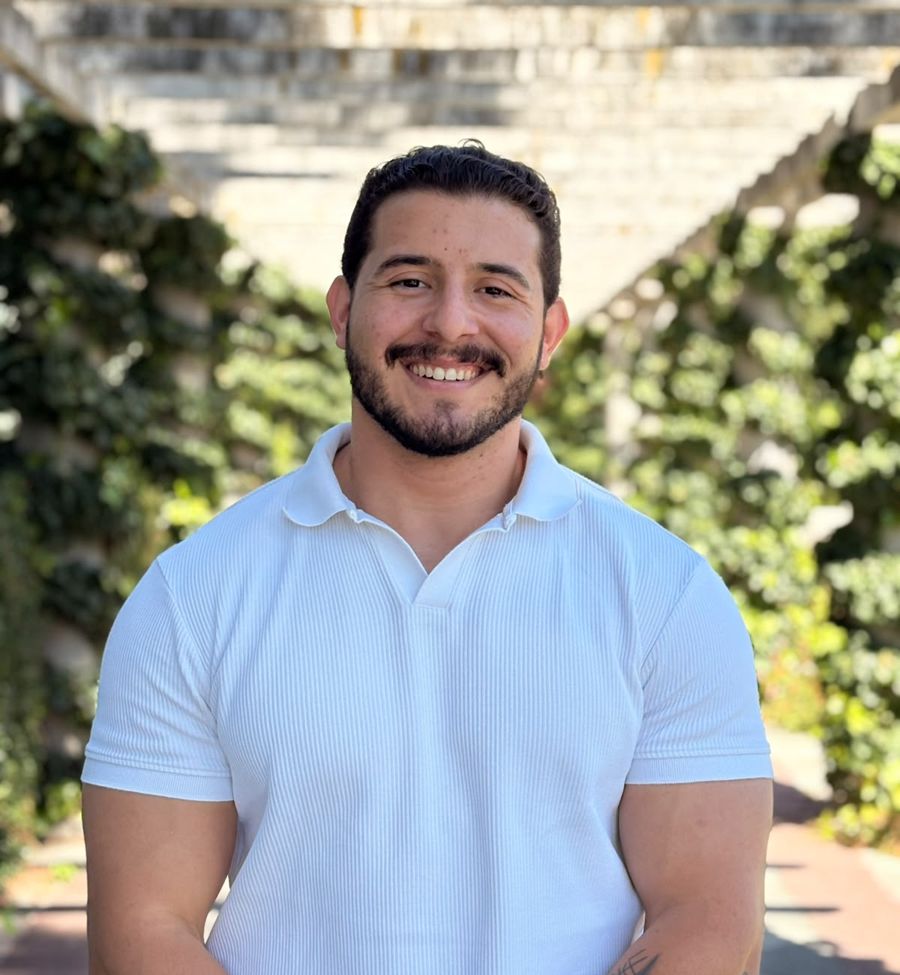 João Cericato sorrindo, de camisa branca, num jardim com hera